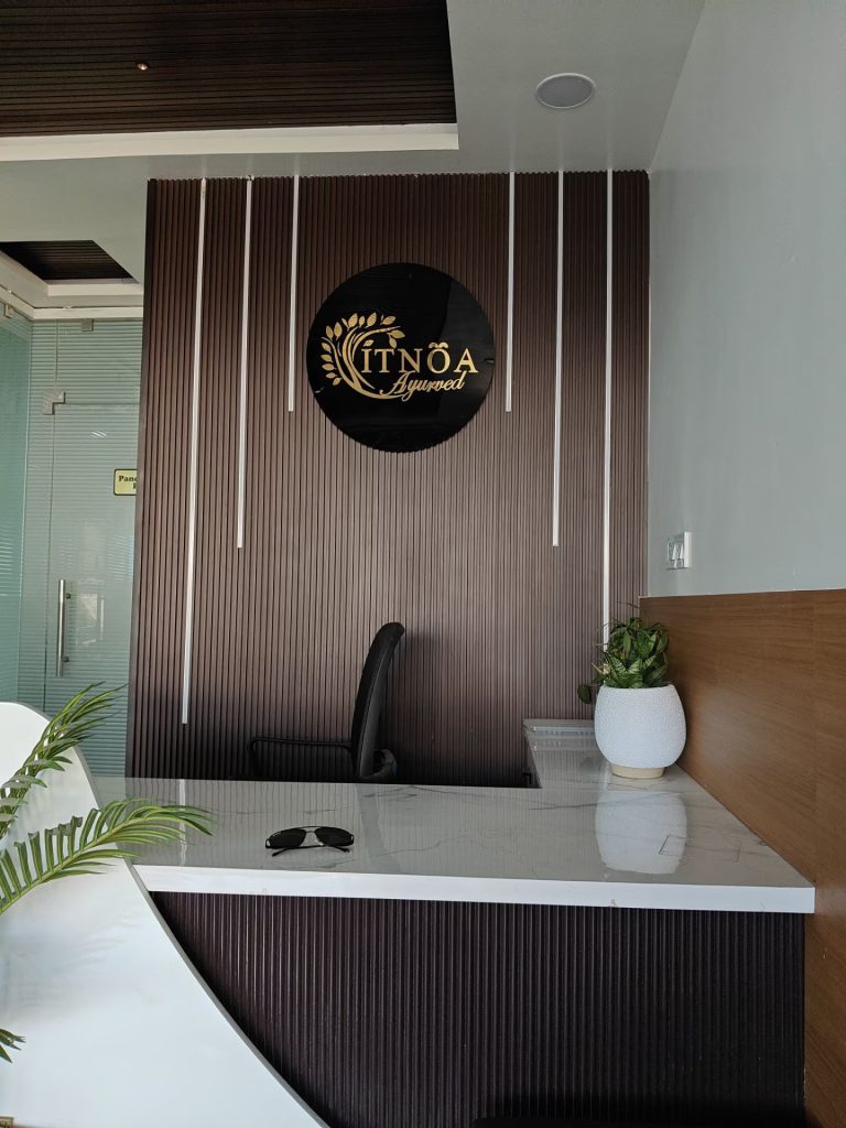 Modern reception desk and ITNOA Ayurved Clinic wall emblem inside the clinic